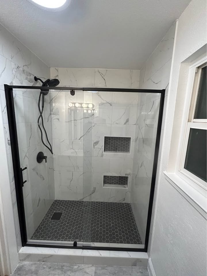 Baño remodelado con regadera de azulejo tipo mármol y marco negro