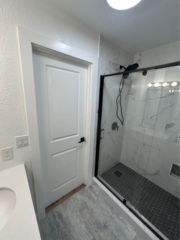 Baño remodelado con regadera de azulejo y puerta de vidrio